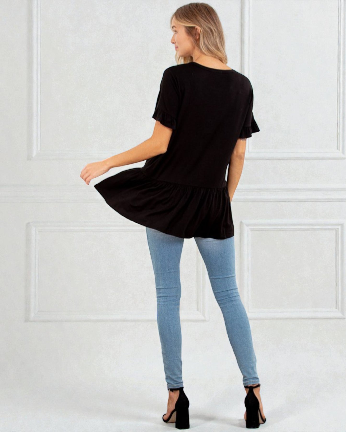 Woman wearing a black oversized t-shirt and light blue jeans against a white wall.