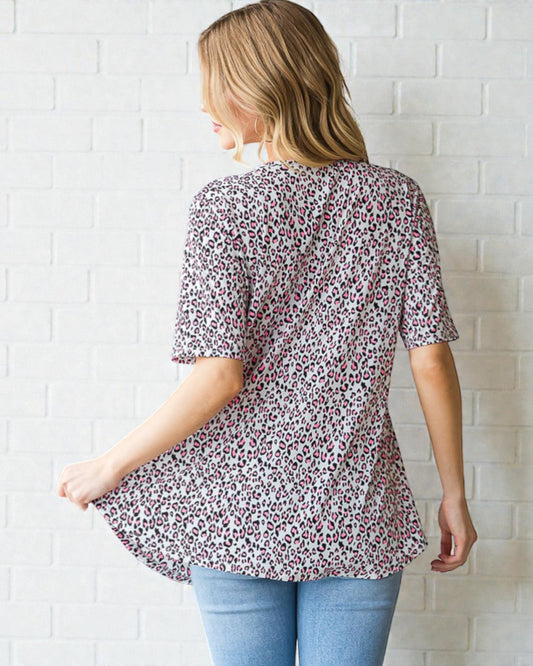 Woman wearing a floral blouse and blue jeans against a white brick wall.