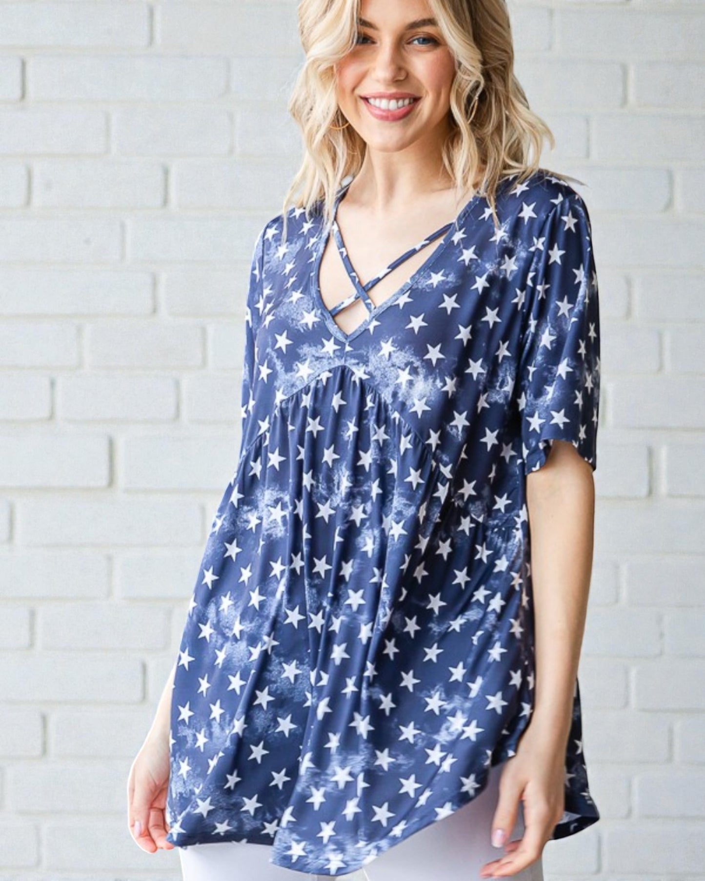 Woman wearing a blue star-patterned top against a white brick wall.