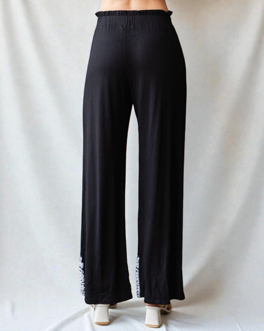 Black wide-leg pants with white fringe details on a plain background
