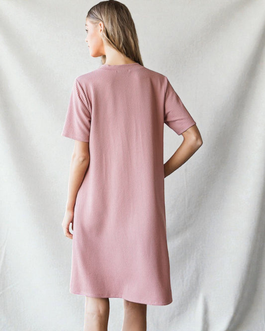 Woman wearing a pink ribbed dress against a plain background