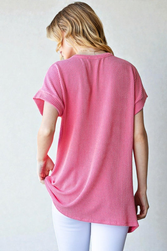 Woman wearing a pink ribbed tunic over white pants on a plain background