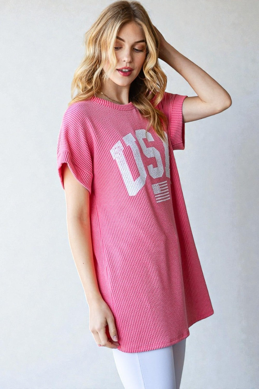 Woman wearing a pink t-shirt with 'USA' print on a plain background
