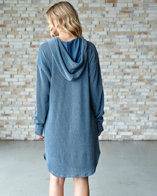 Woman wearing a blue hooded dress against a brick wall.