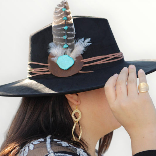 Black hat with feather and turquoise stone decoration worn by a person.
