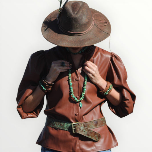 Person wearing a brown leather outfit with a hat, necklace, and belt on a white background