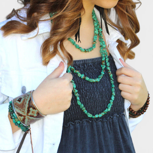 Person wearing a green beaded necklace and holding a phone, with a plain background
