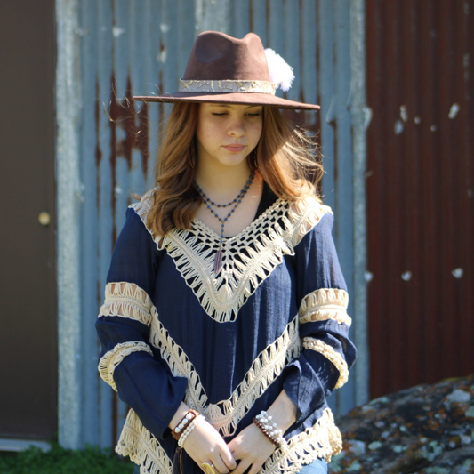Woman wearing a blue poncho with white lace and a brown hat against a rustic metal wall.