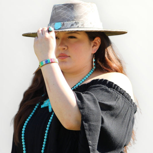 Woman wearing a gray hat and black top with turquoise jewelry against a white background