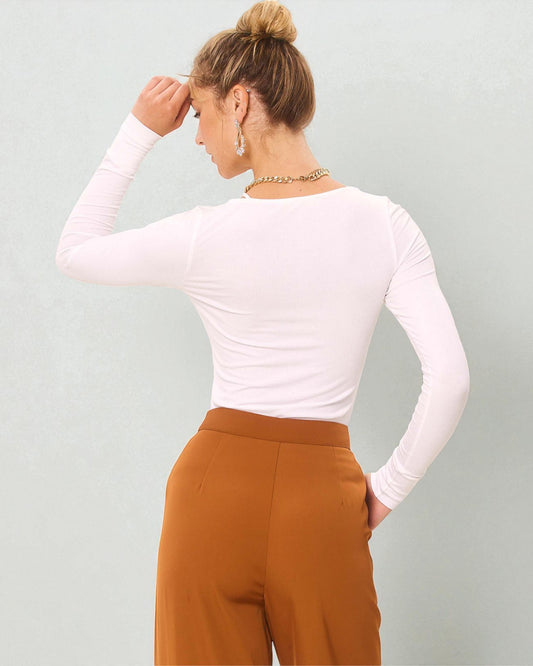 Person wearing a white long-sleeve top and brown pants against a light gray background