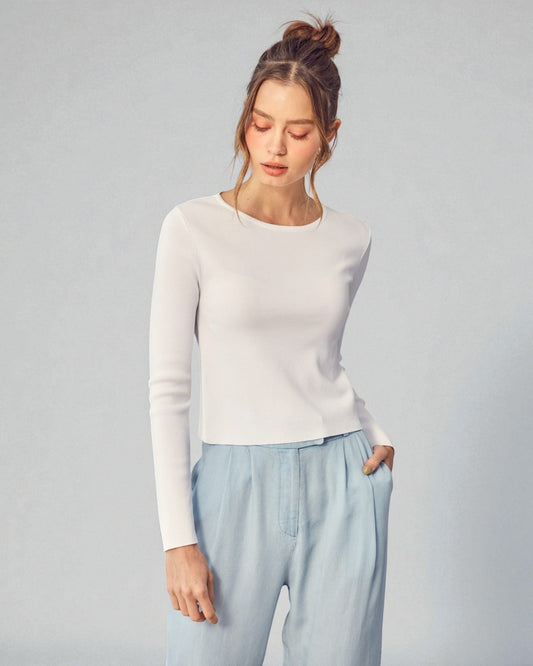 Woman wearing a white sweater and light blue pants against a gray background