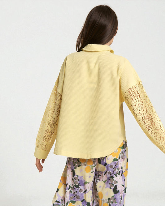 Woman wearing a yellow embroidered jacket with floral pants on a white background