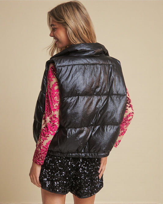 Person wearing a black puffer vest over a colorful floral shirt with a beige background