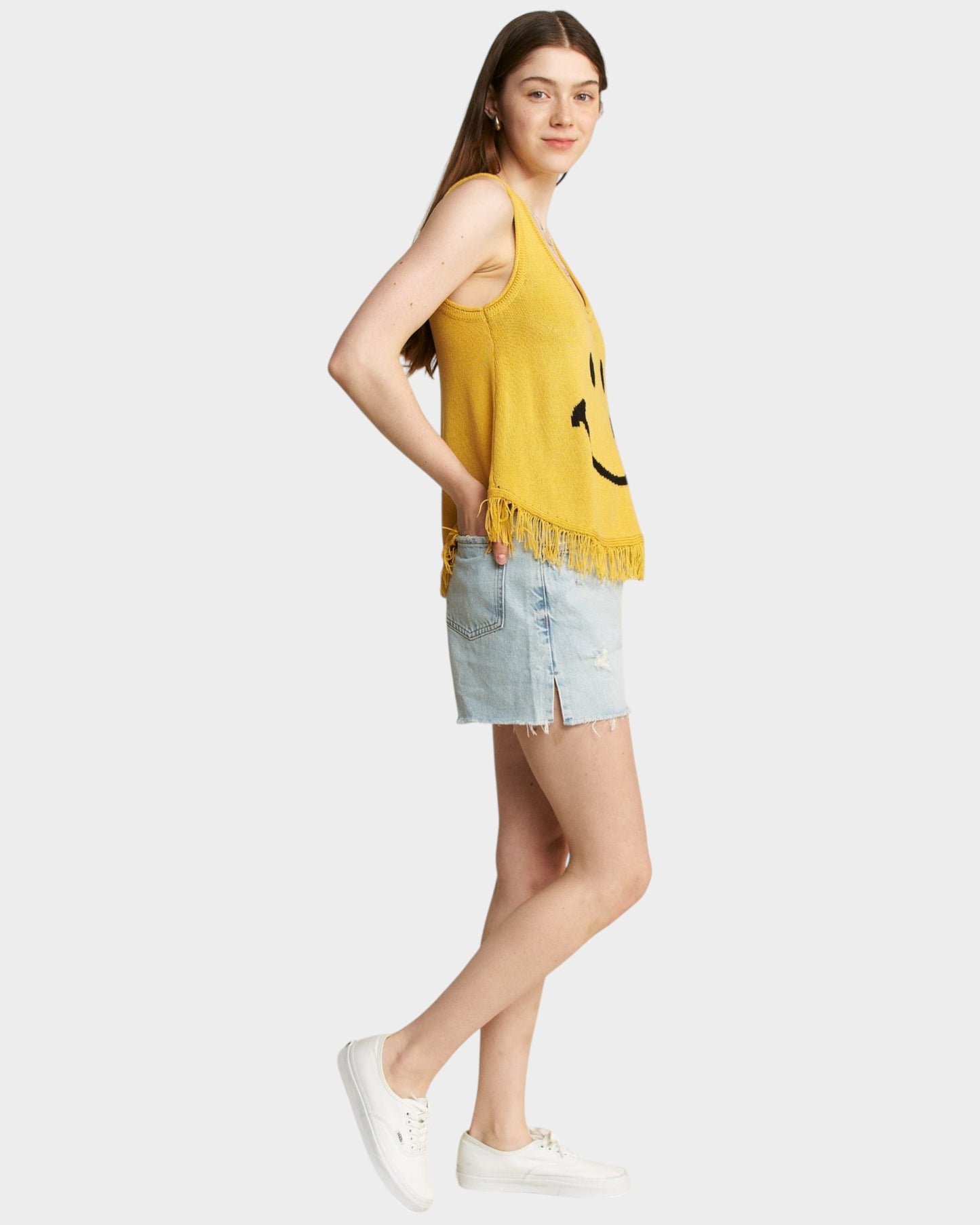 Woman wearing a yellow sleeveless top with a smiley face design and denim shorts on a white background
