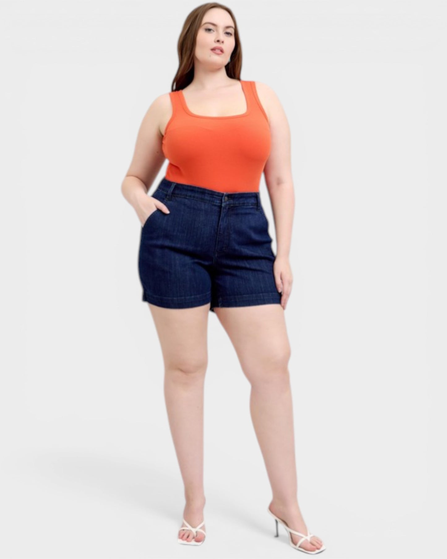Woman wearing an orange tank top and blue shorts on a white background