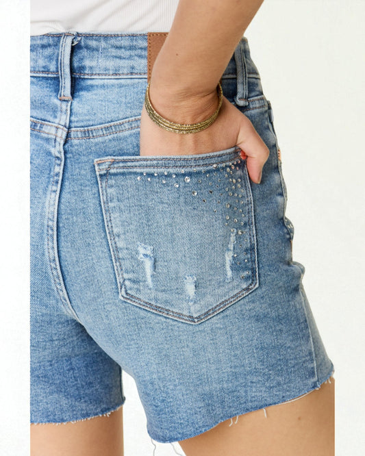 Close-up of a person wearing distressed denim shorts on a white background