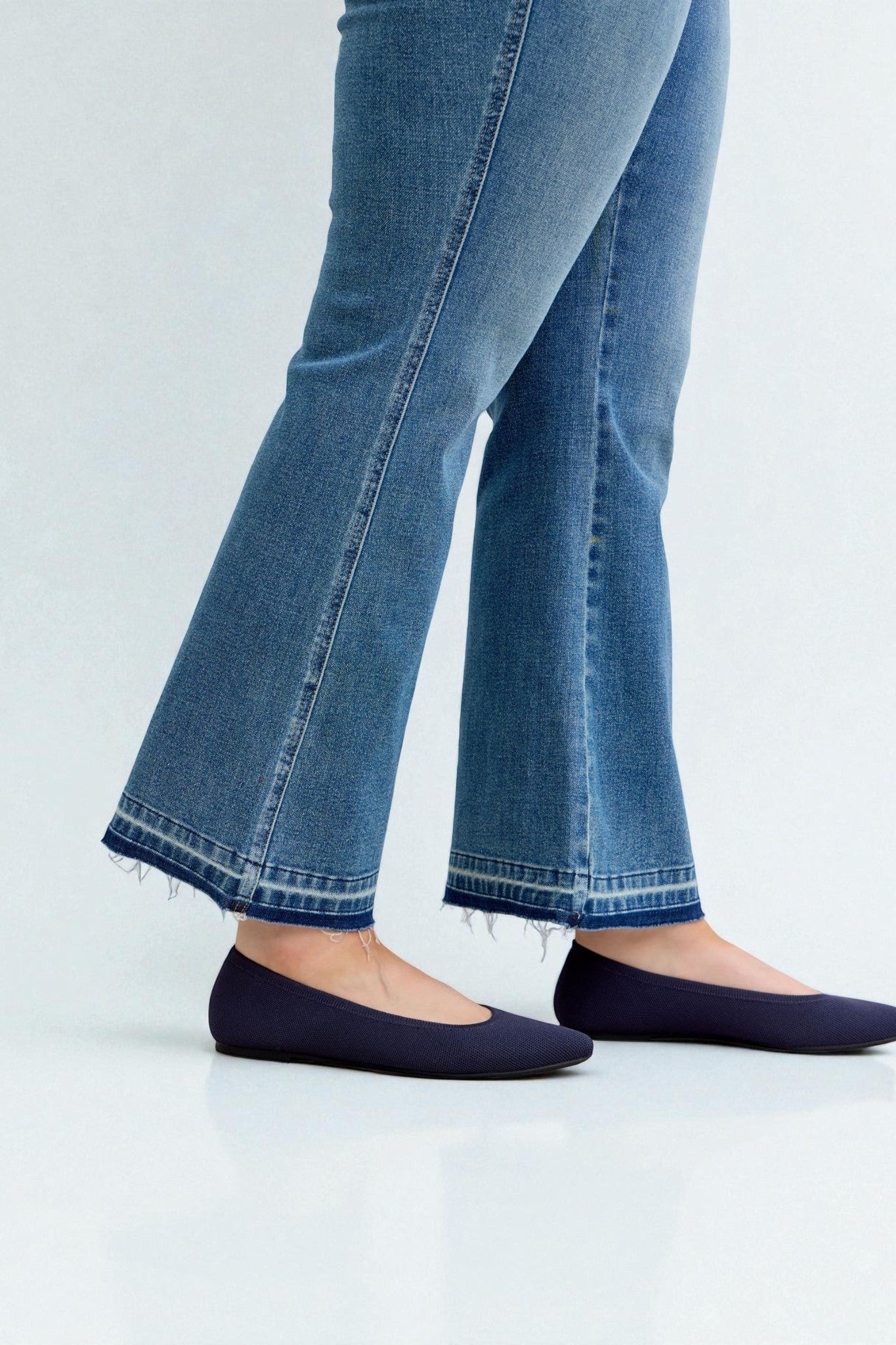 Person wearing blue jeans and navy flats on a light gray background