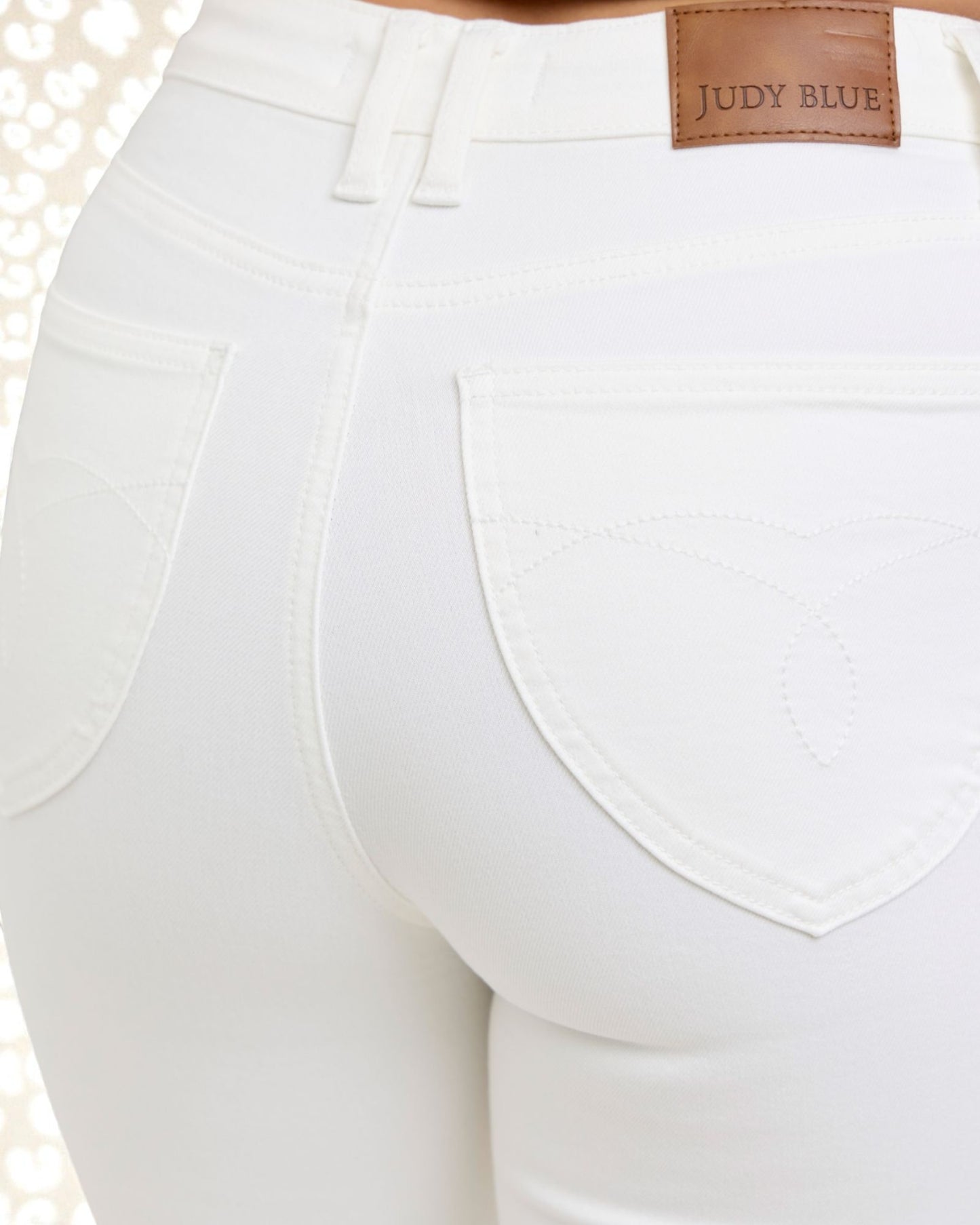 Close-up of white pants with a 'Judy Blue' label on a blurred background