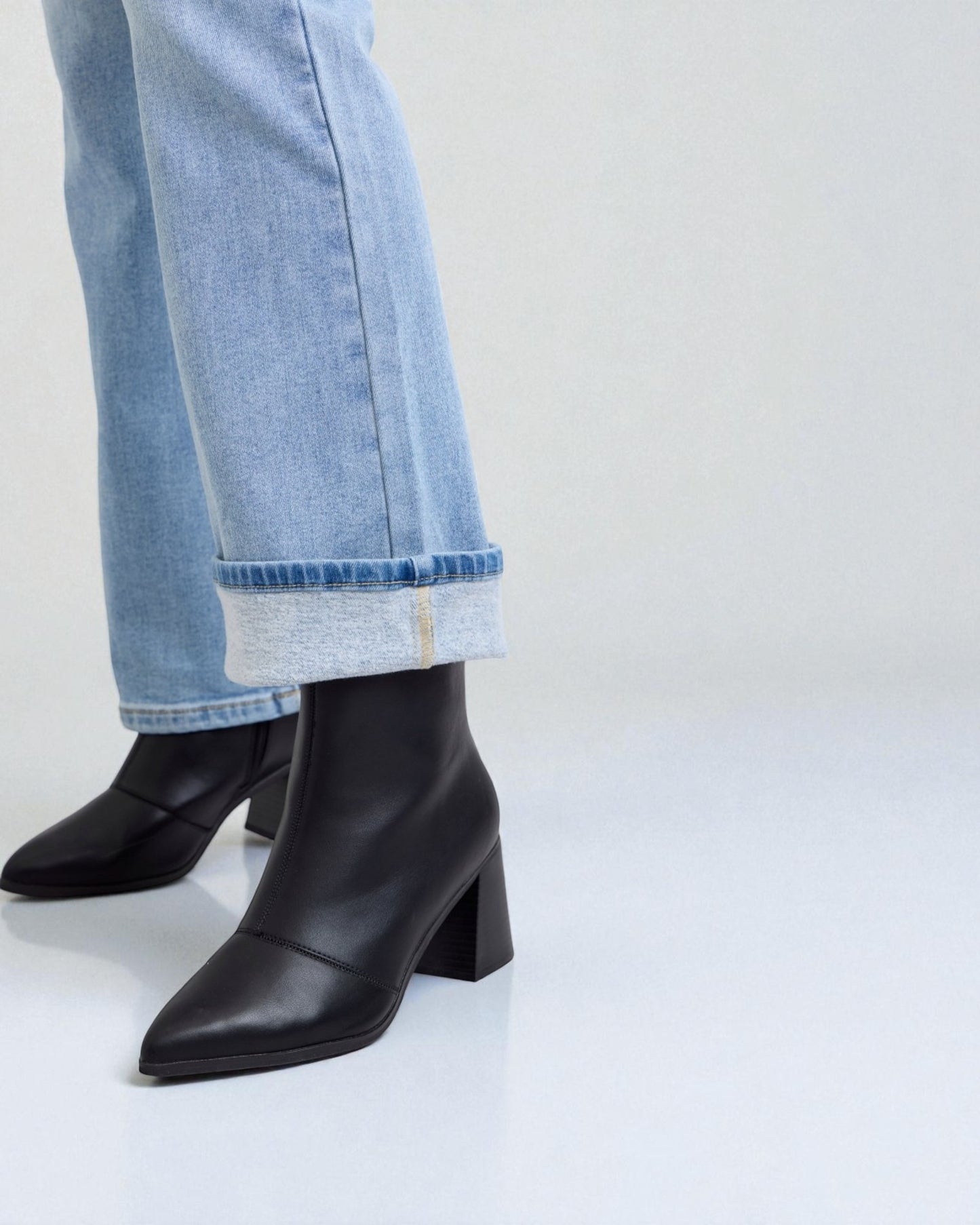 Black heeled boots worn with light blue jeans on a white background