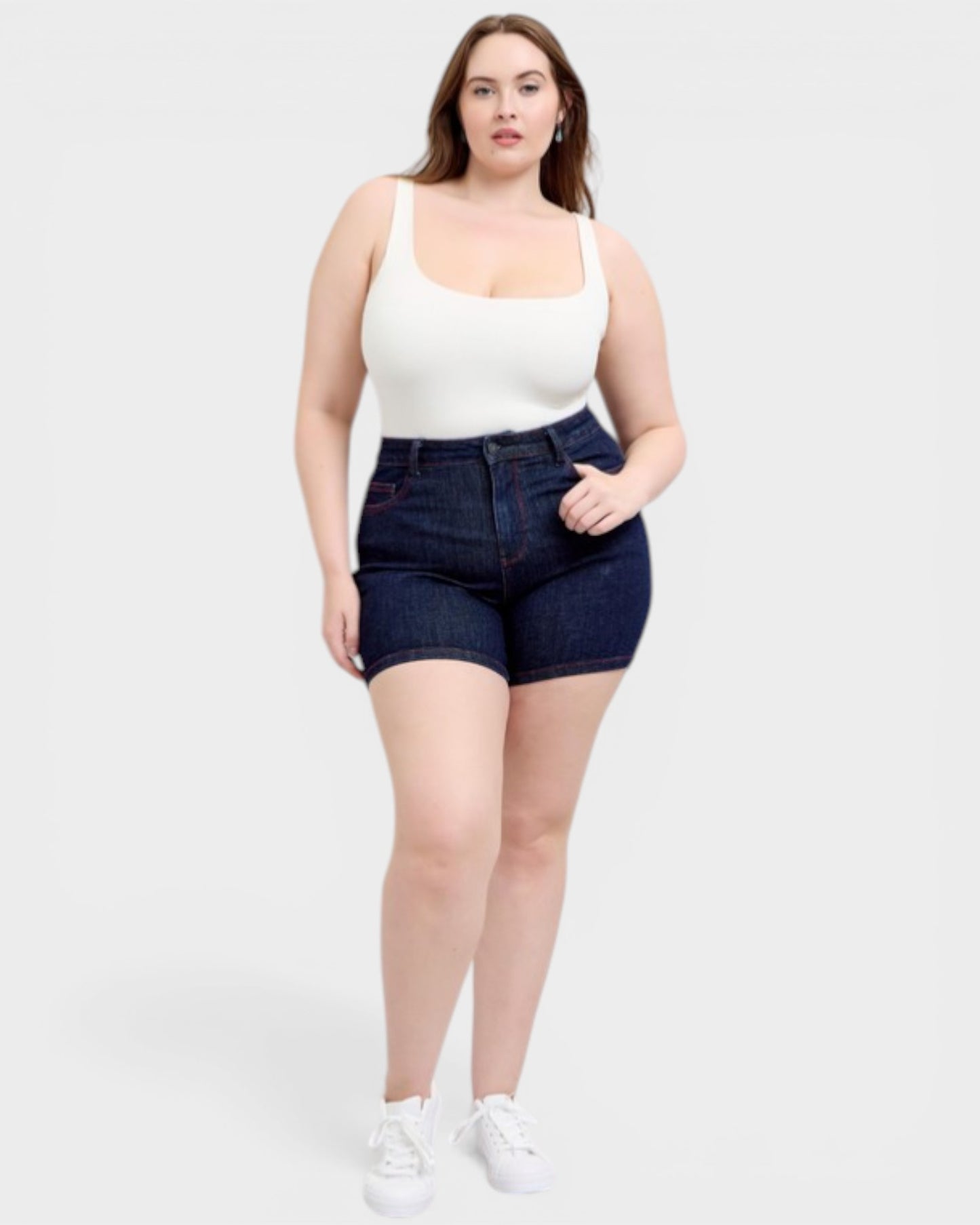 Woman wearing a white tank top and dark blue denim shorts on a white background