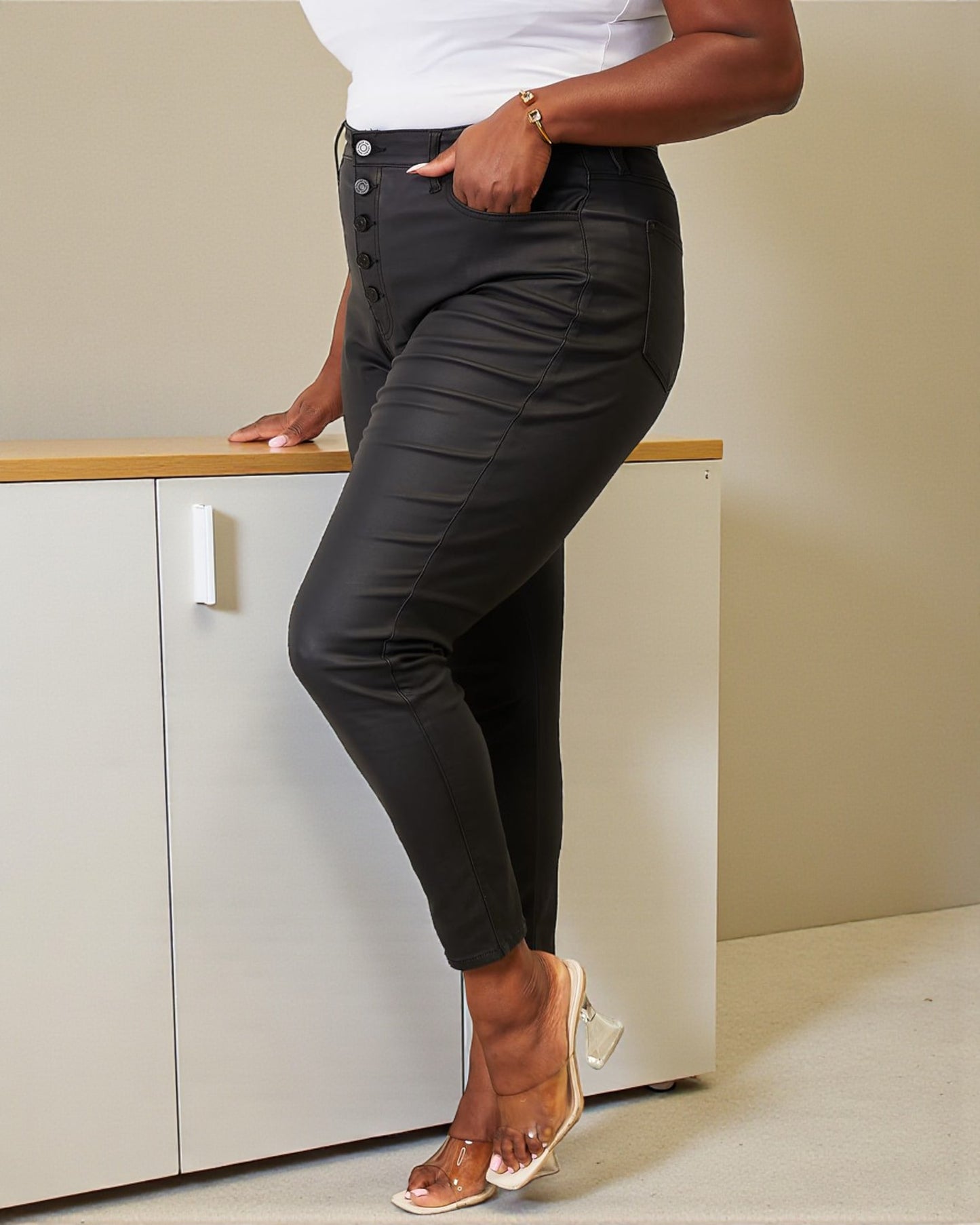 Person wearing dark gray pants with button details, standing in a minimalistic room.