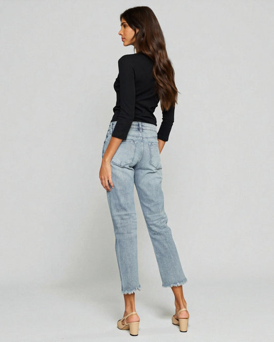 Woman wearing light blue jeans and a black top on a plain background