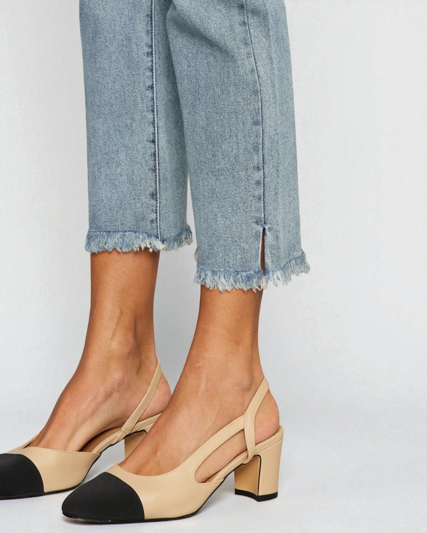 Beige and black slingback heels worn with light blue jeans on a white background
