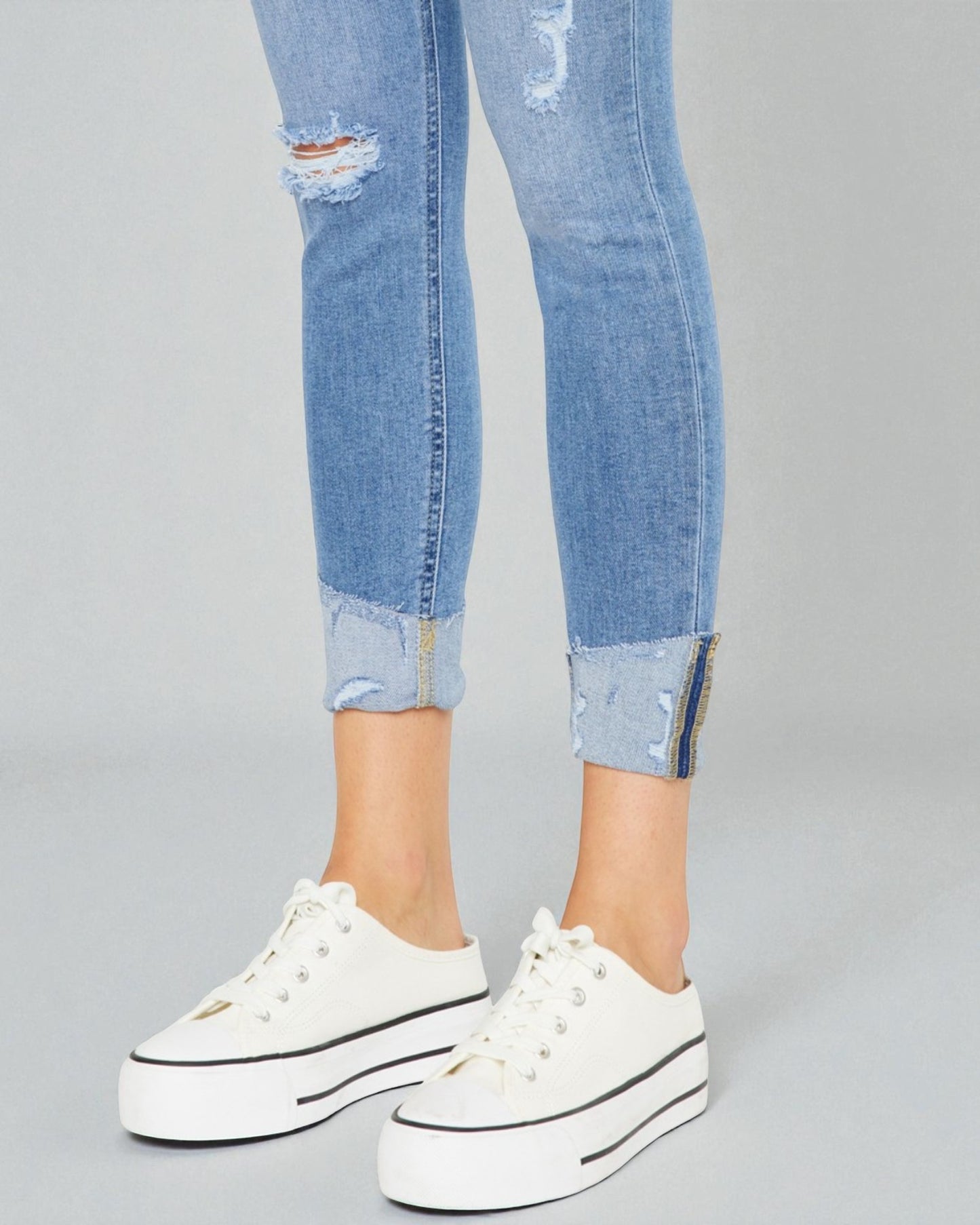 Ripped blue jeans with rolled-up cuffs and white sneakers on a gray background