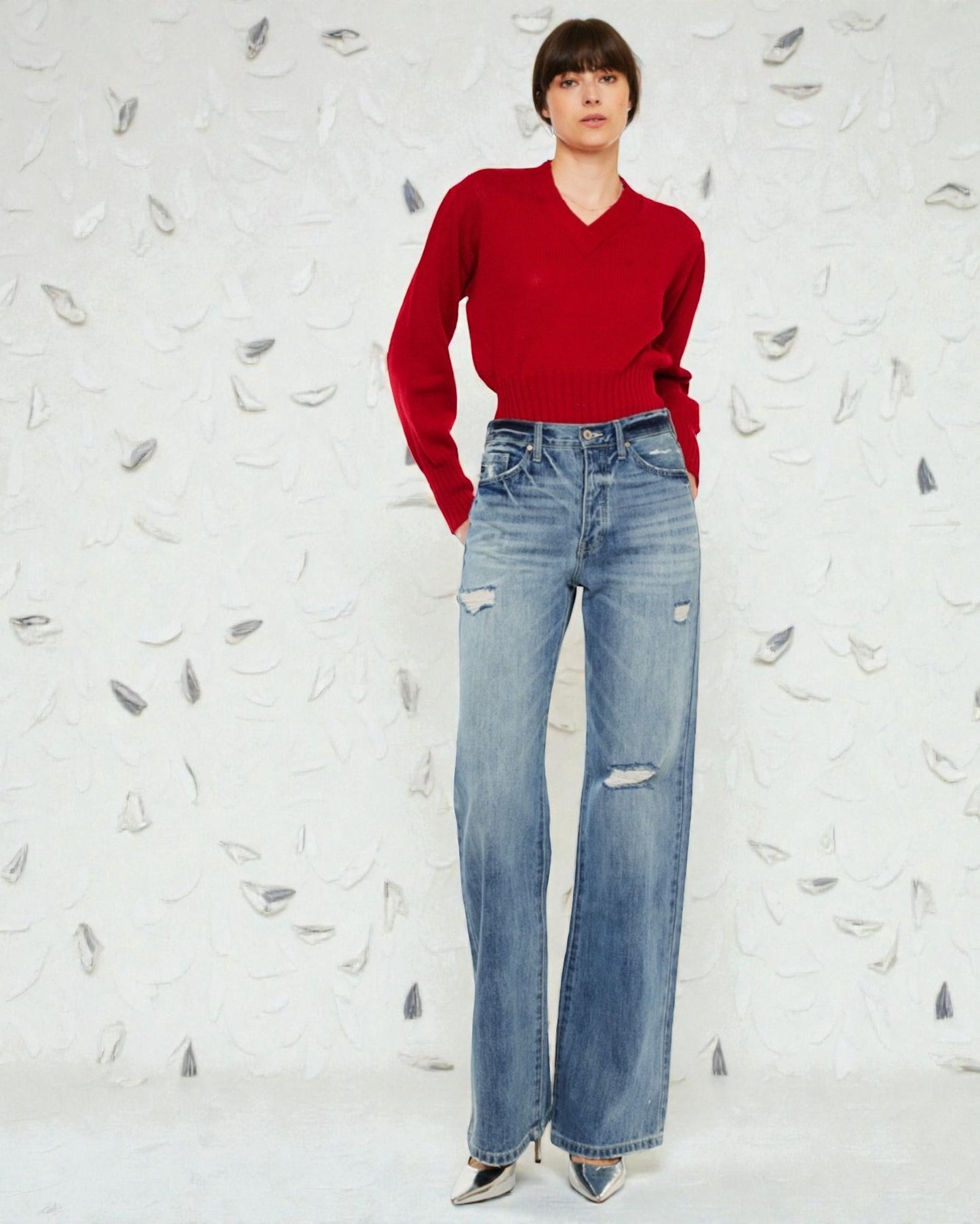Person wearing a red sweater and blue jeans against a textured white background