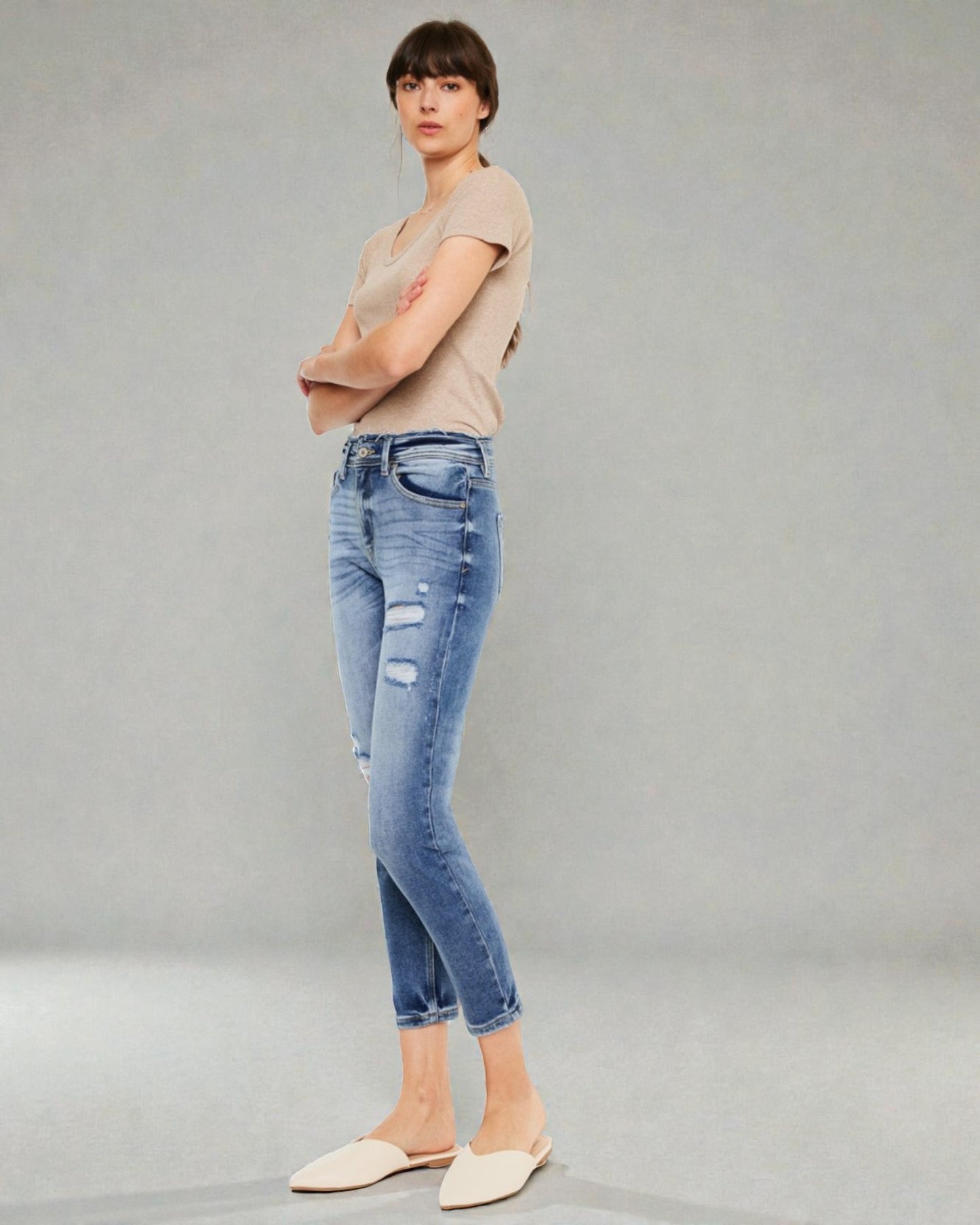 Woman wearing a beige top and blue jeans on a gray background