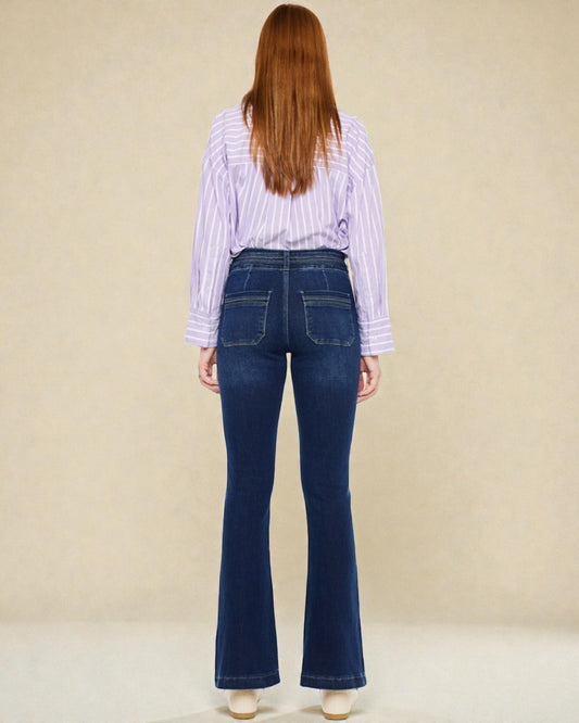 Person wearing blue flared jeans and a striped shirt from behind on a beige background