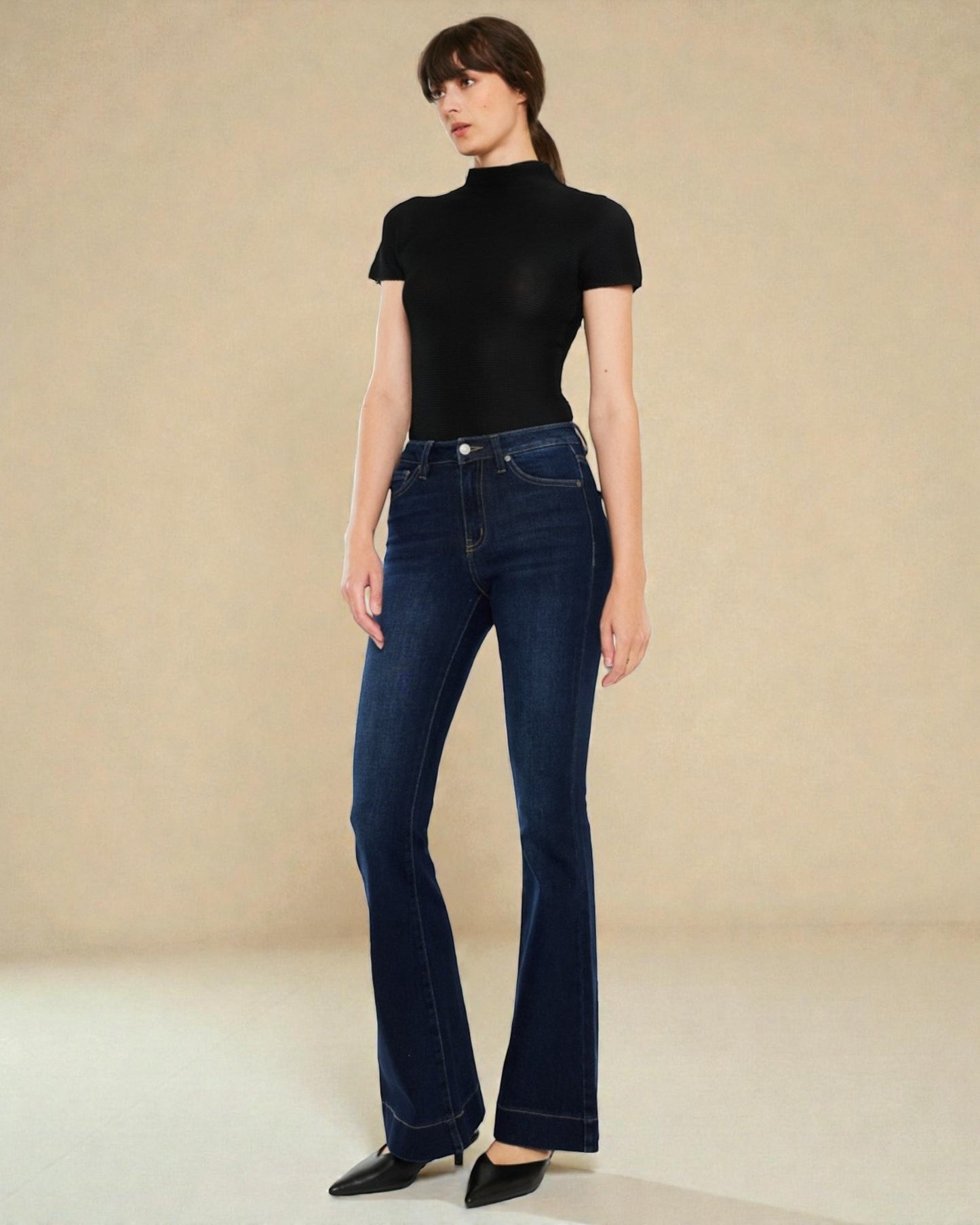 Woman wearing a black turtleneck and dark blue jeans on a beige background