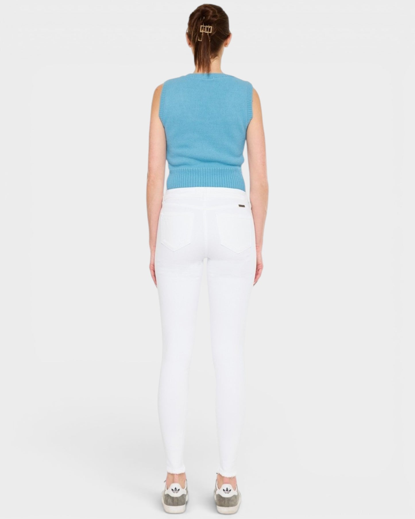 Person wearing a blue sleeveless top and white pants on a light gray background