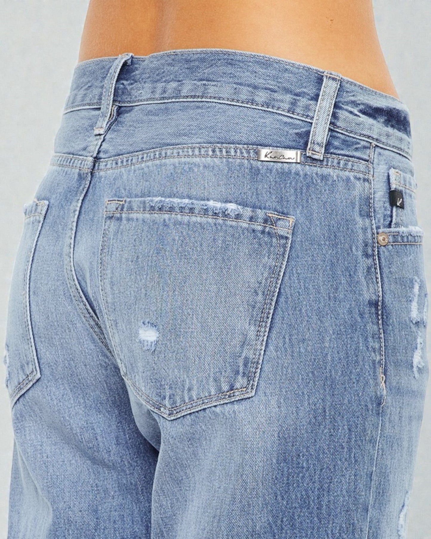 Close-up of a person wearing light blue jeans with a gray background