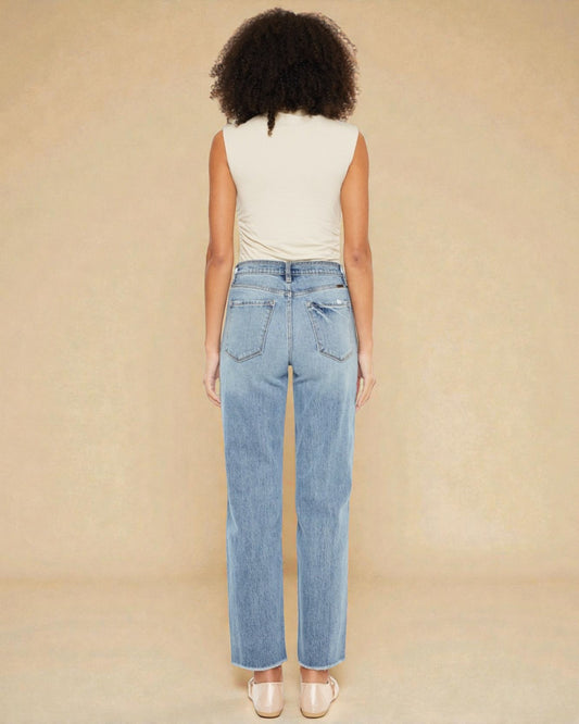 Person wearing light blue jeans and a white top on a beige background