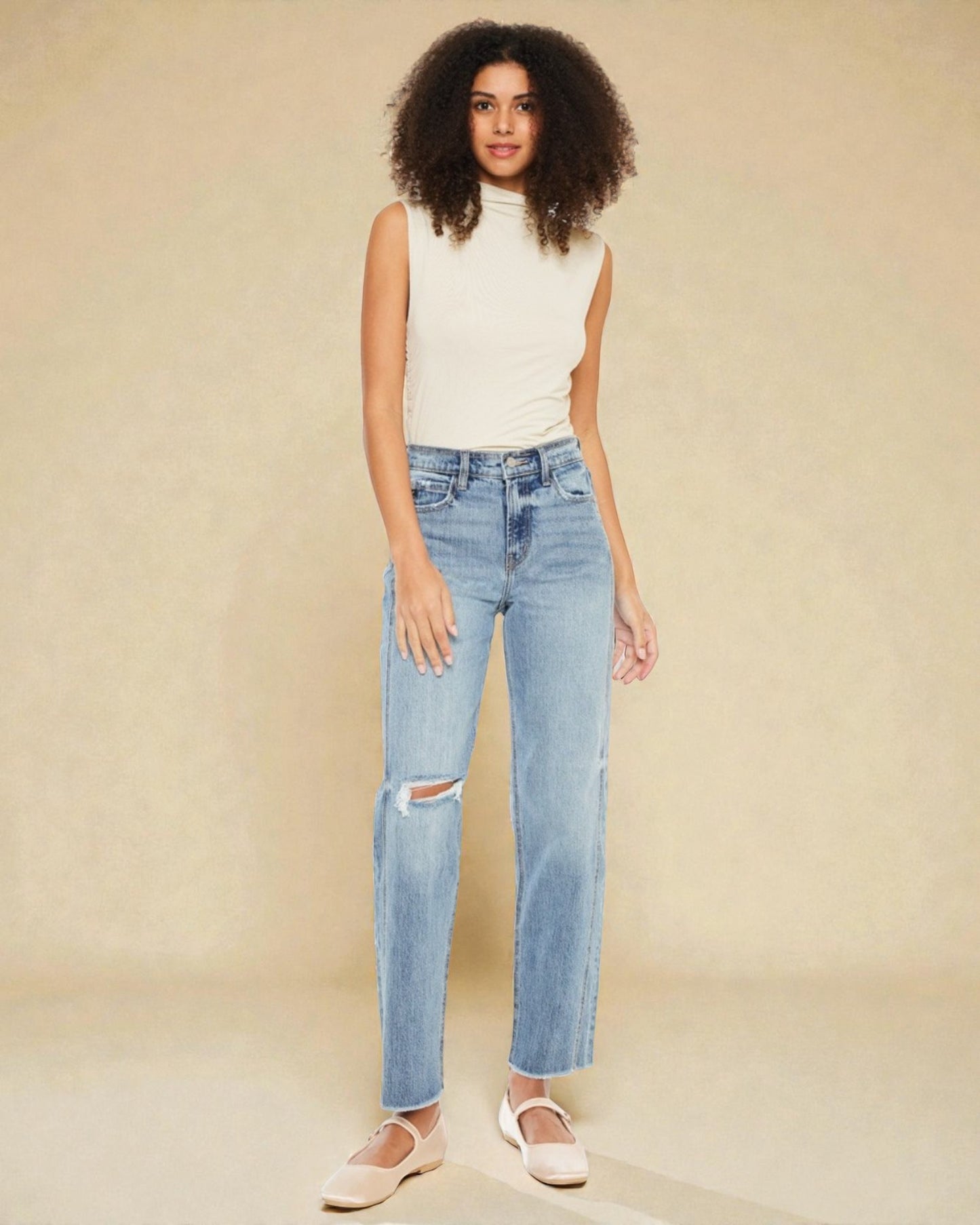 Woman wearing light blue jeans with a distressed knee on a beige background