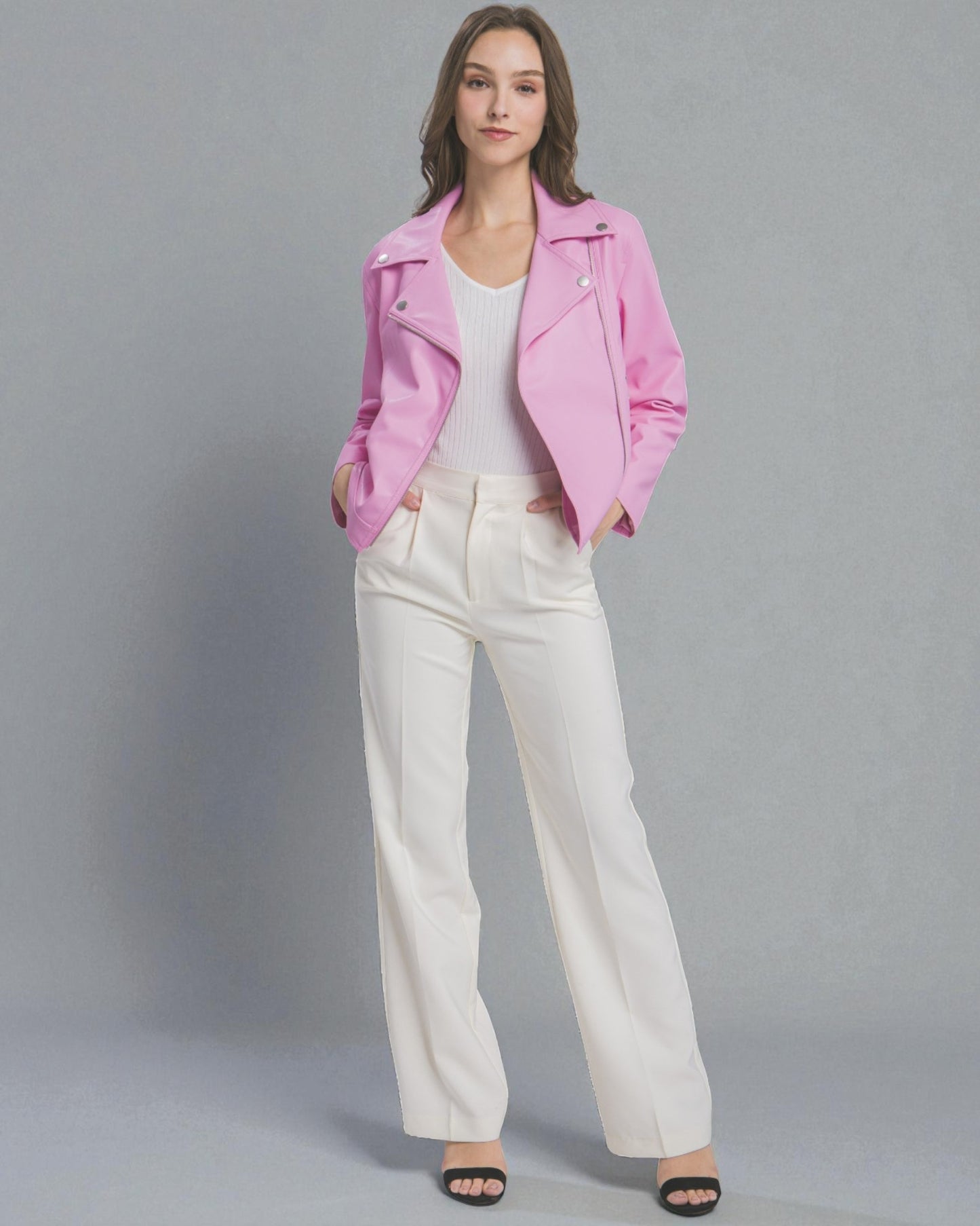 Woman wearing a pink jacket and white pants on a gray background