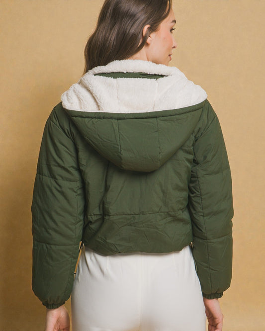 Green puffer jacket with white fur lining worn by a person on a beige background