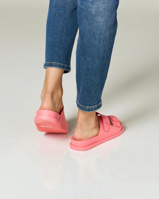 Person wearing pink slip-on shoes and blue jeans on a plain background