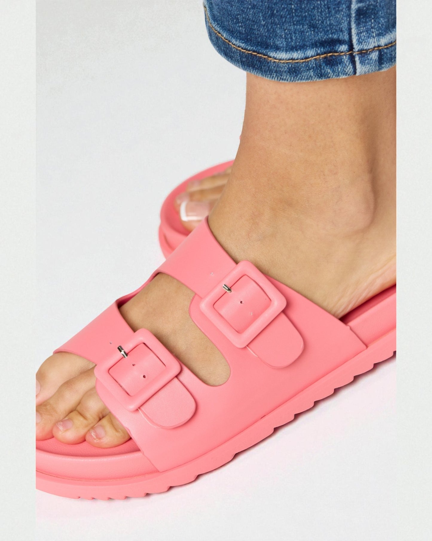 Pink sandals with buckles worn by a person on a white background