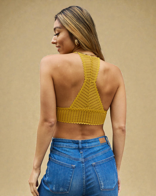 Woman wearing a mustard yellow knitted crop top and blue jeans on a beige background