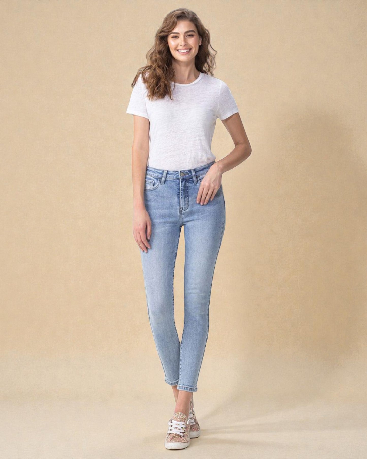 Woman wearing light blue jeans and a white t-shirt on a beige background
