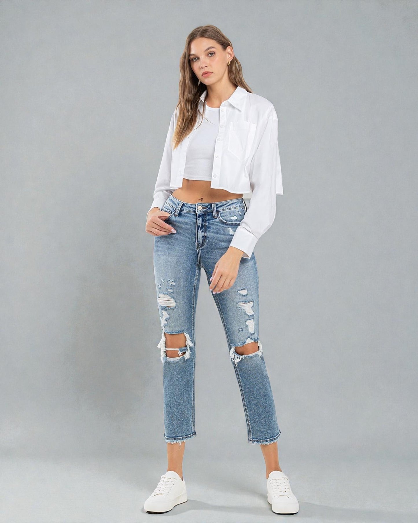 Woman wearing a white blouse and distressed jeans on a gray background