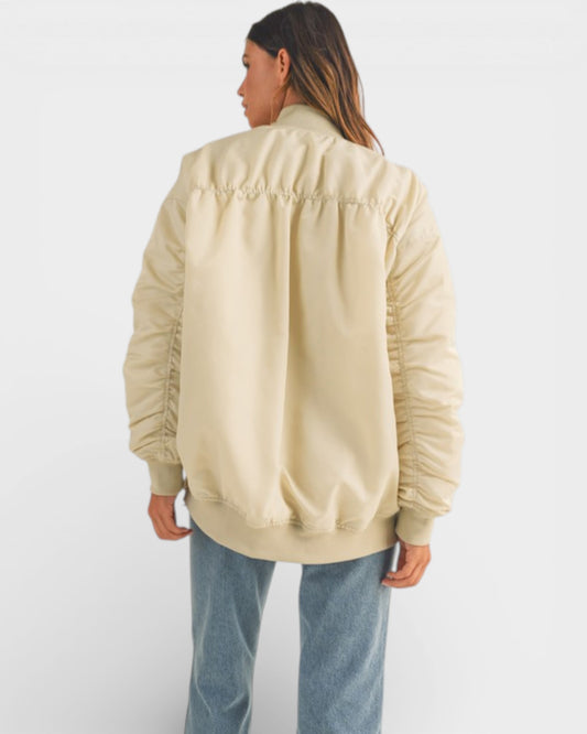 Person wearing a beige bomber jacket and blue jeans on a white background