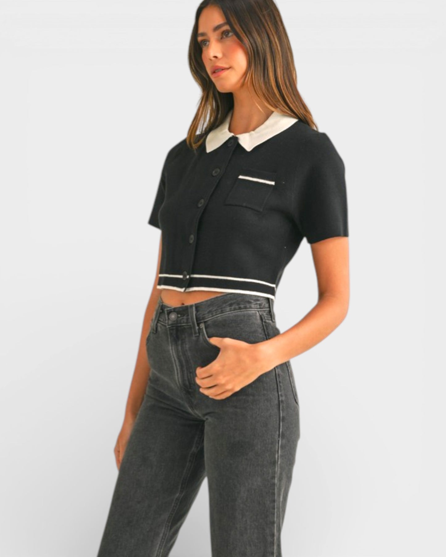 Woman wearing a black and white cropped top with high-waisted jeans on a plain background