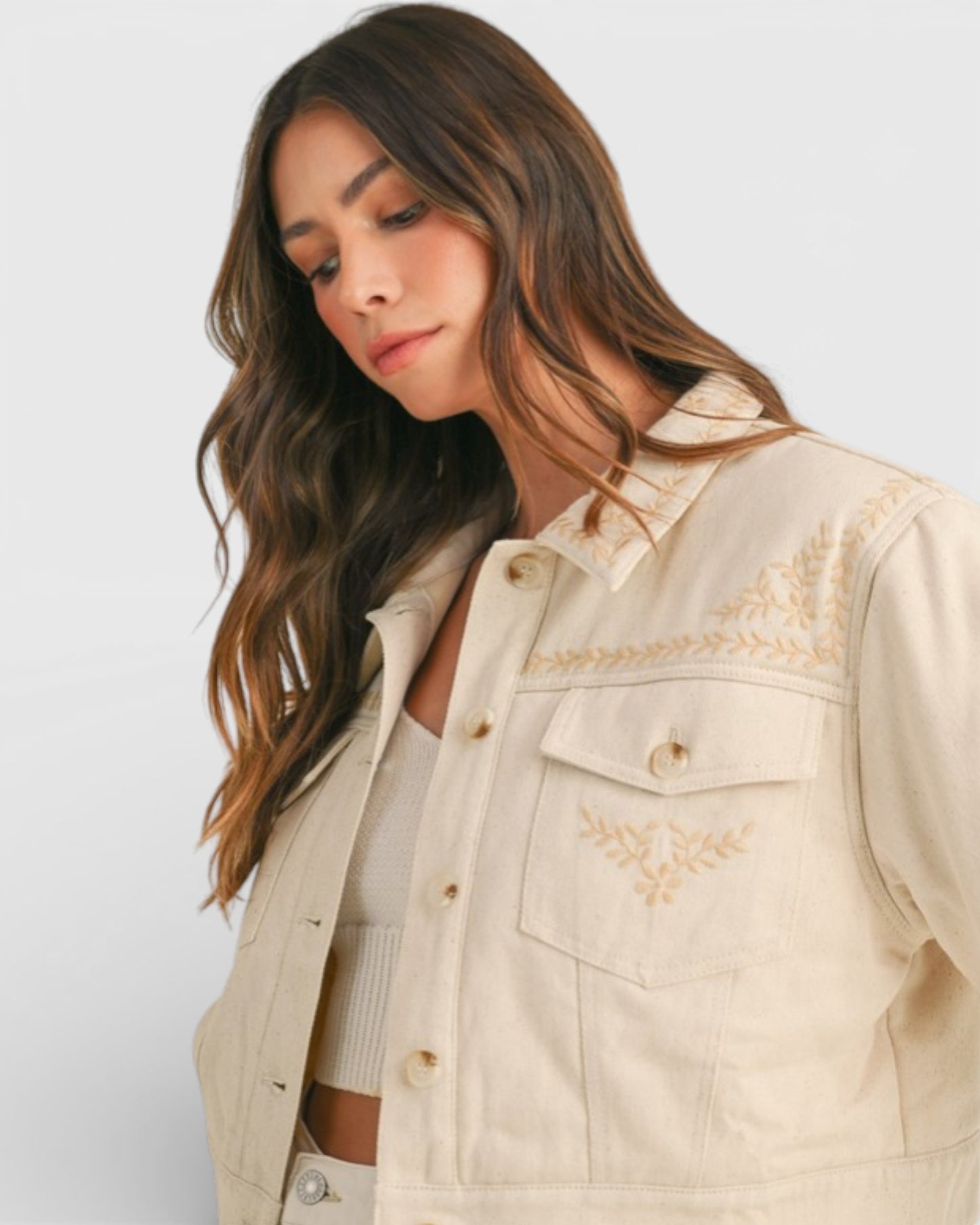 Woman wearing a beige jacket with gold embroidery on a white background