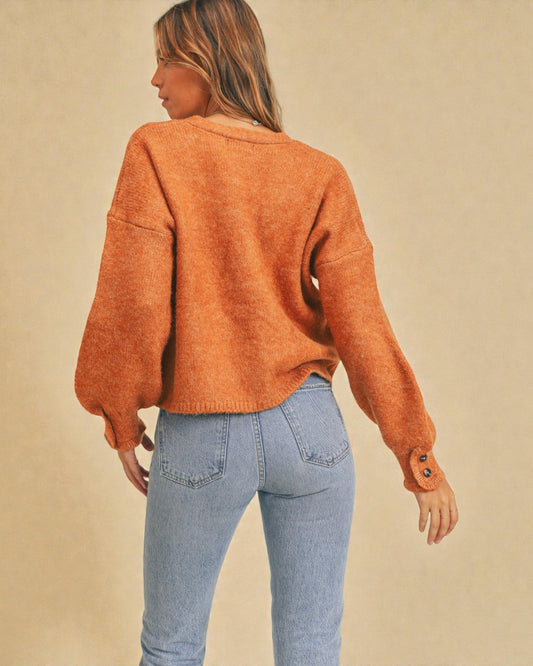 Person wearing an orange sweater and light blue jeans on a beige background
