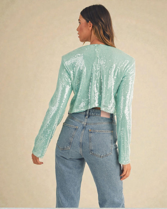Person wearing a light green sequin top and blue jeans on a beige background