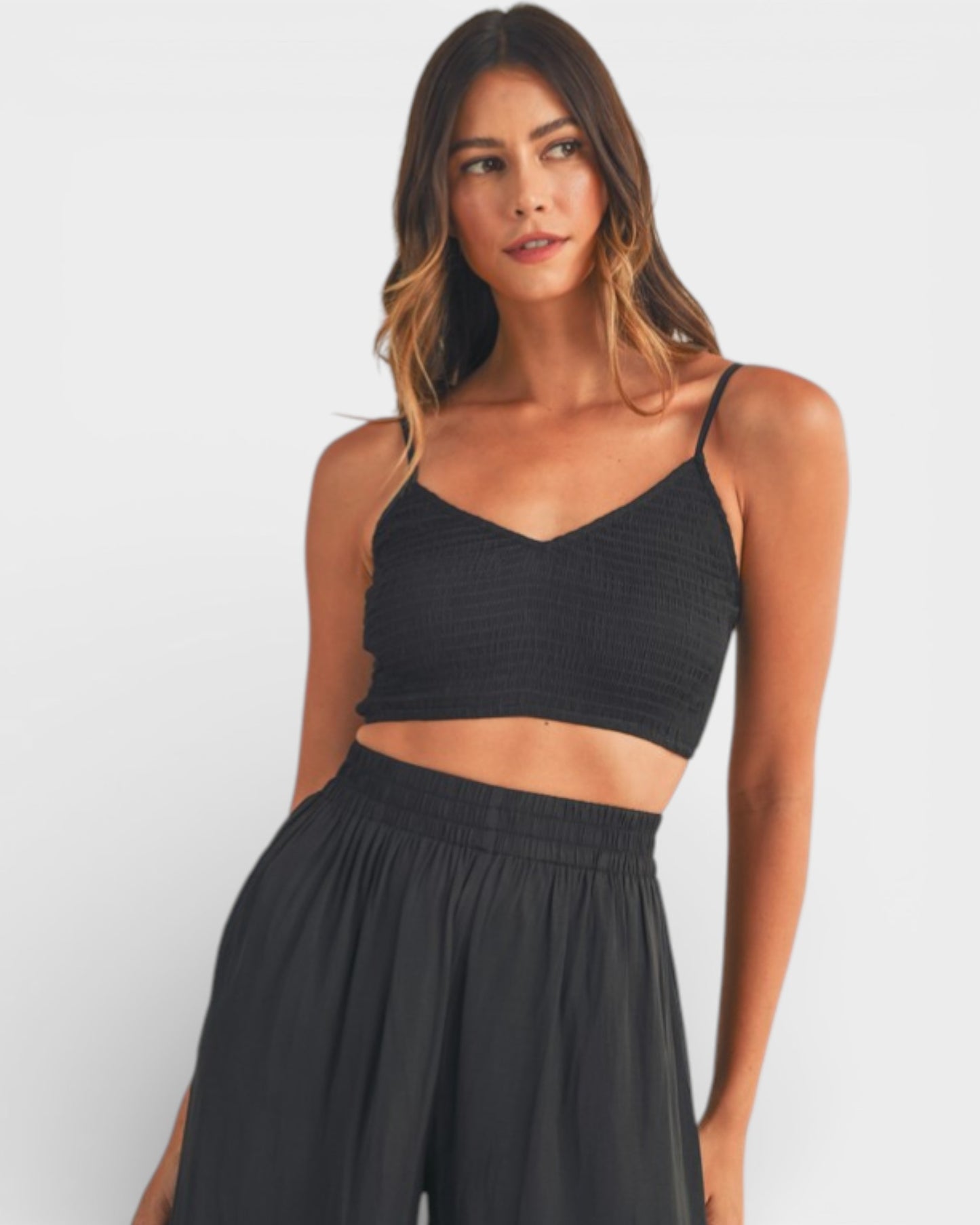 Woman wearing a black crop top and wide-leg pants on a white background