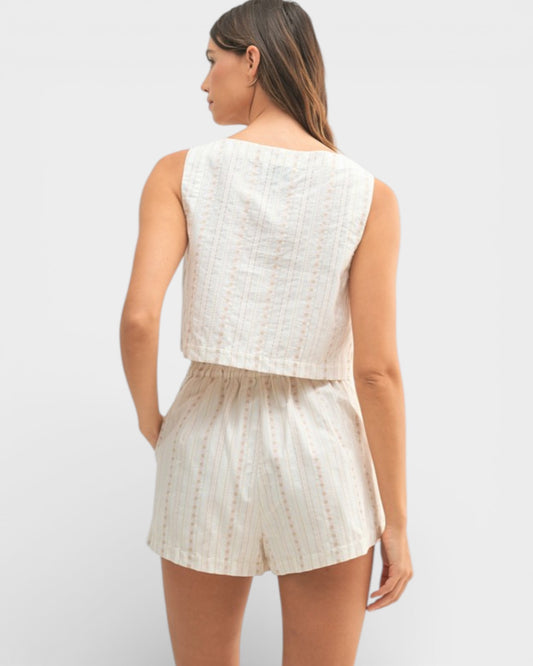 Woman wearing a white sleeveless top and shorts set on a light gray background